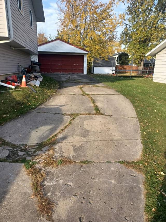 Before: cracked, settled concrete driveway with weeds growing through the joints, prior to replacement